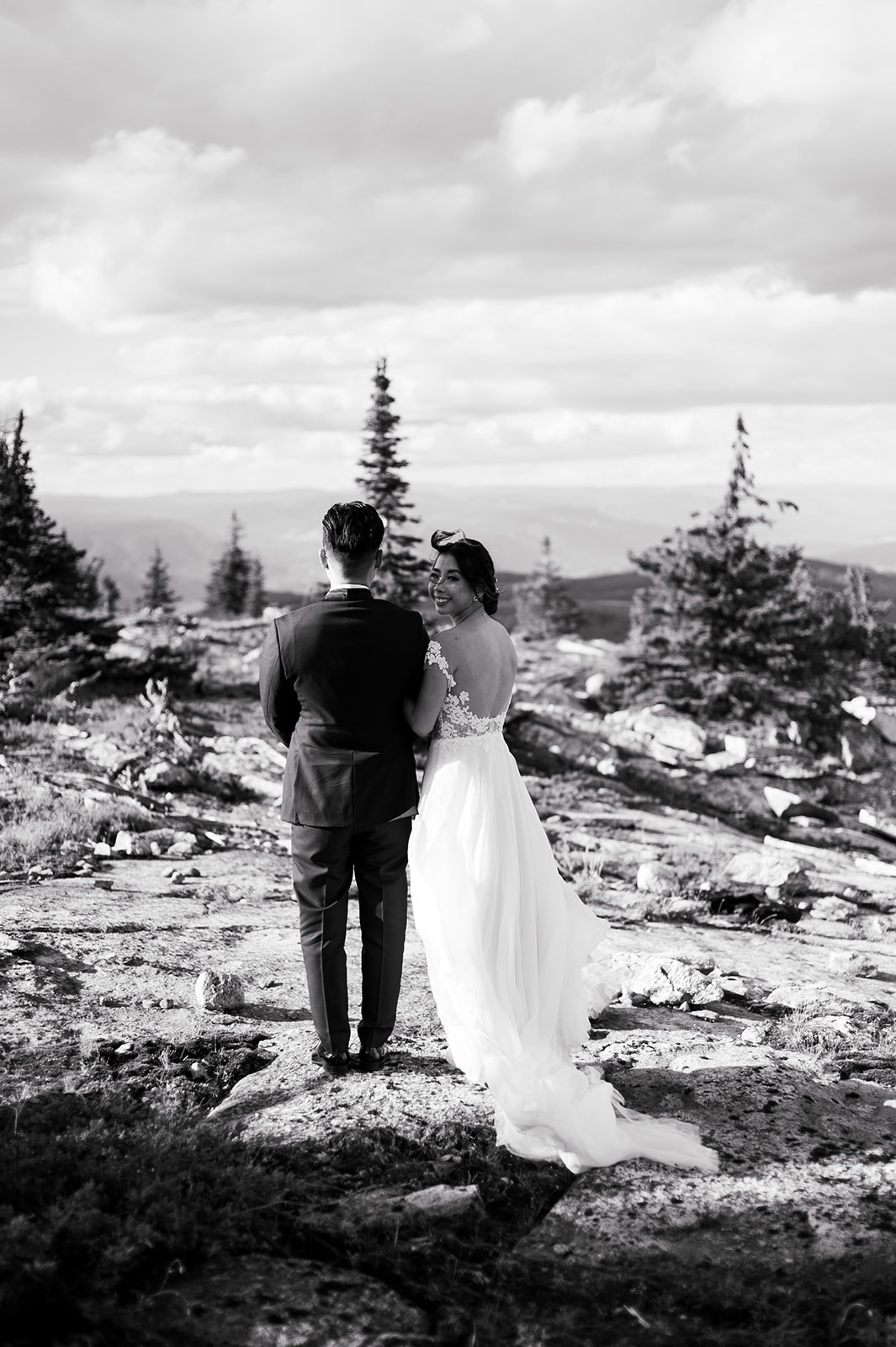 Bride and groom stand on a cliff's edge on their wedding day.